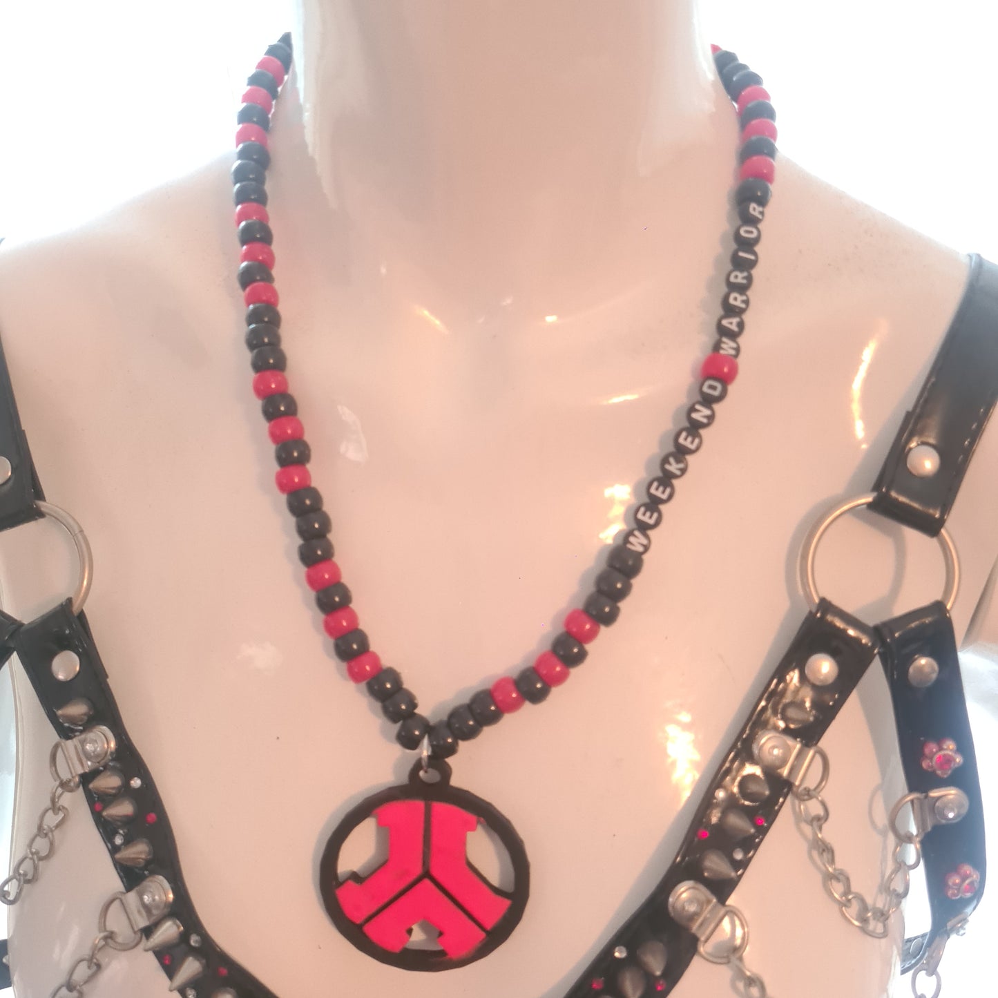 Black leather harness with red and black beaded chain on a mannequin bust.