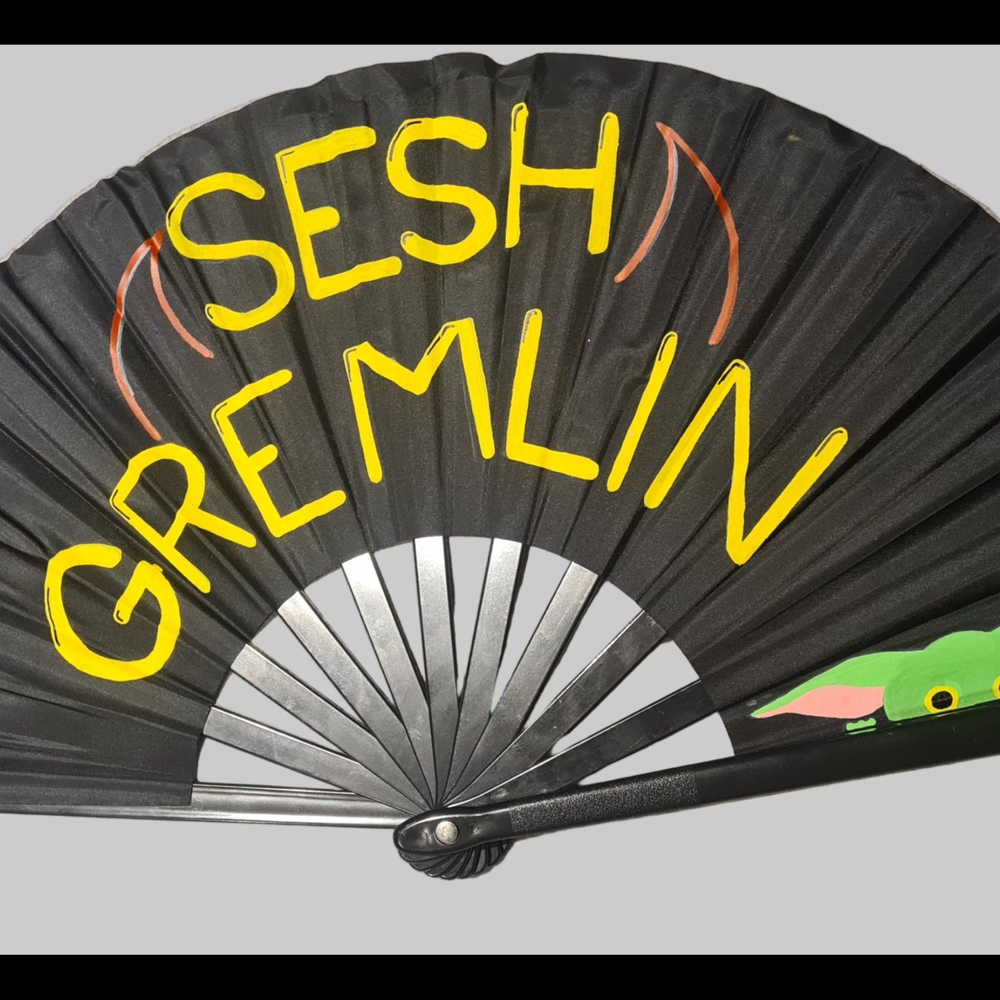 Sesh Gremlin UV Fan, black handpainted with yellowi lettering, red devil horns anda green gremlin, UV reactive for festivals and raves