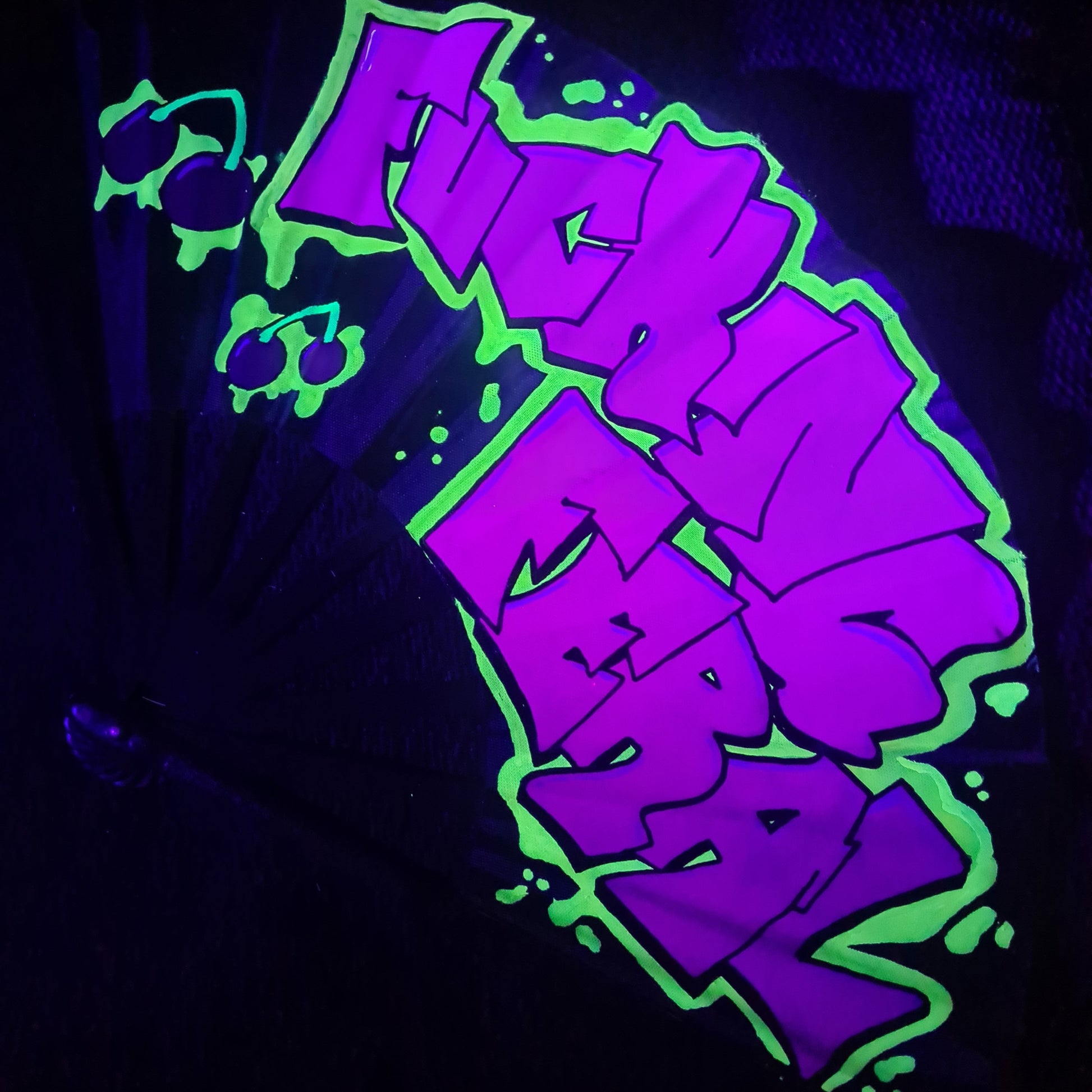 Fucking Feral UV Fan, black handpainted with purple graffiti lettering, yellow outline and red cherries, UV reactive for festivals and raves
