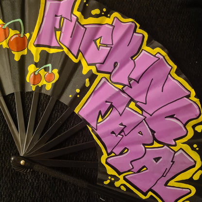 Fucking Feral UV Fan, black handpainted with purple graffiti lettering, yellow outline and red cherries, UV reactive for festivals and raves