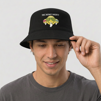 Male model holding the brim of the black Secret Society bucket hat and smiling slightly on a neutral studio background