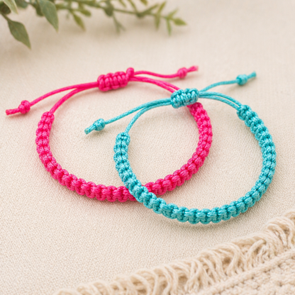 Two braided bracelets, one pink and one blue, on a light beige surface with a natural background.