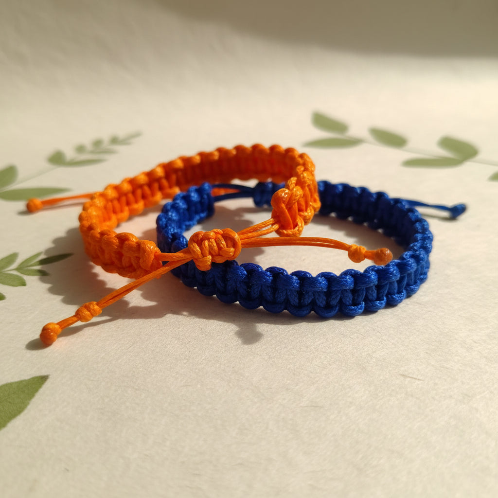 Two braided bracelets, one orange and one blue, on a light background with green leaves.