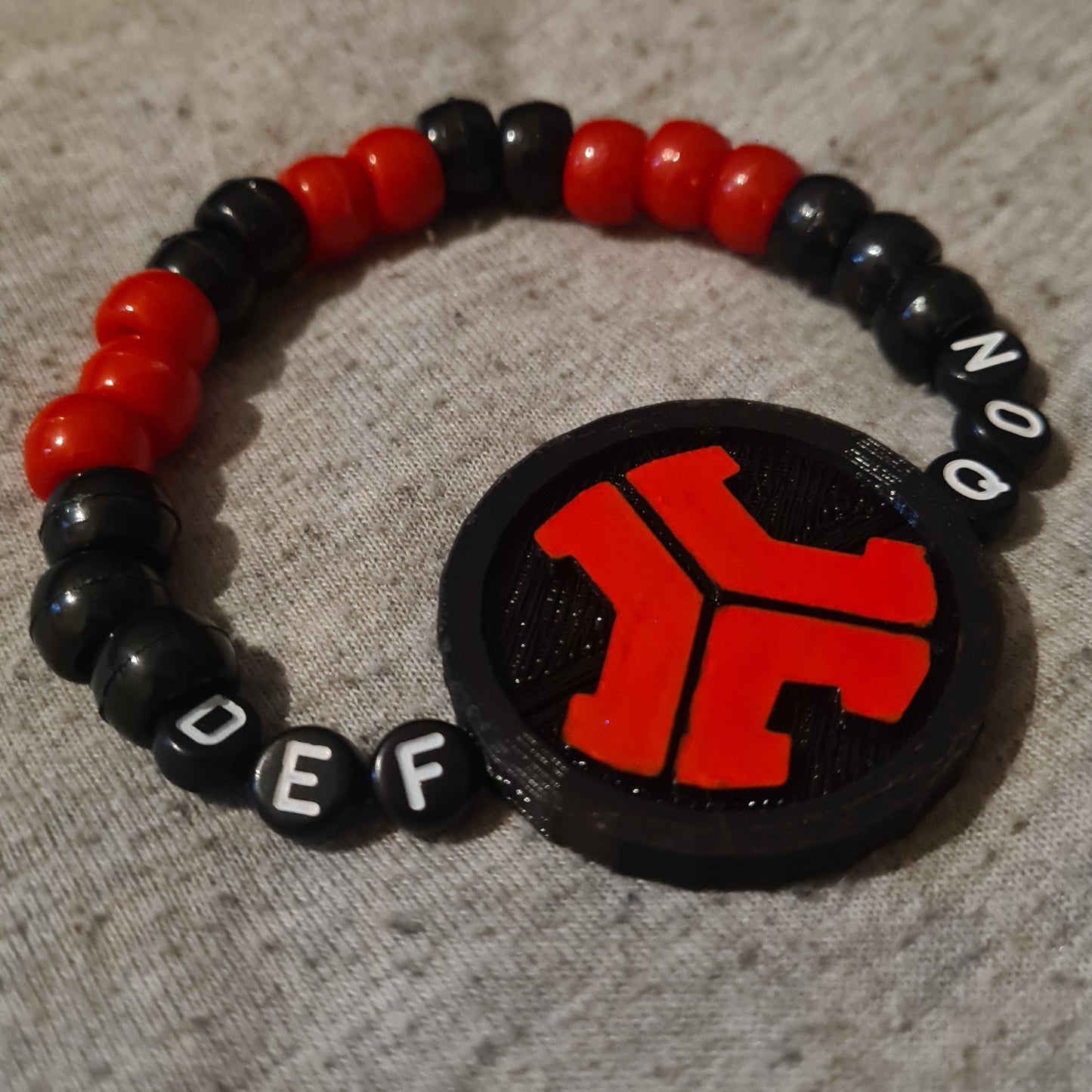 Black and red beaded bracelet with a circular black charm featuring a red symbol on a textured surface.
