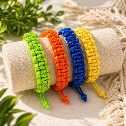 Four colorful braided bracelets on a beige fabric background with green leaves.