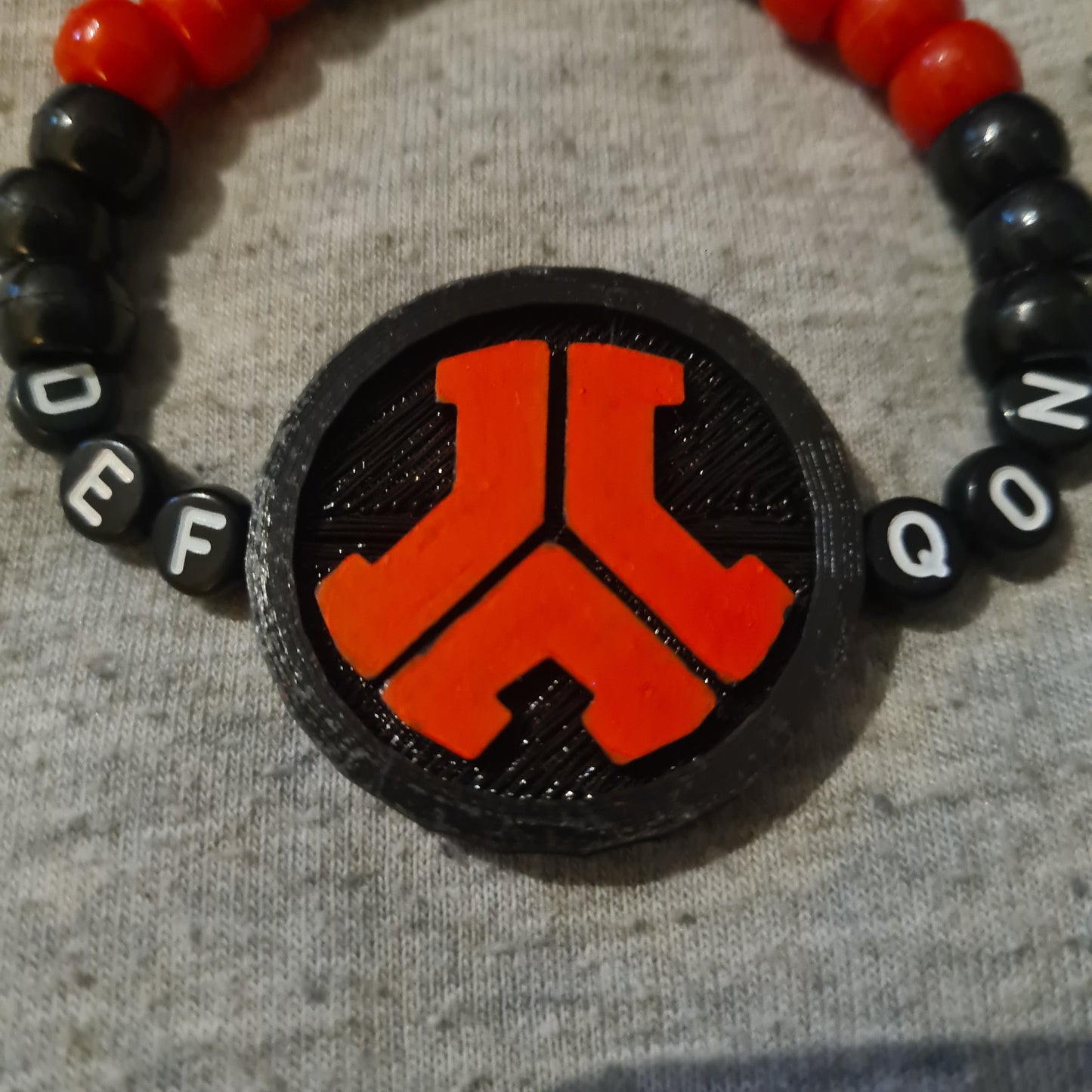 Black and red beaded bracelet with a central emblem on a grey background